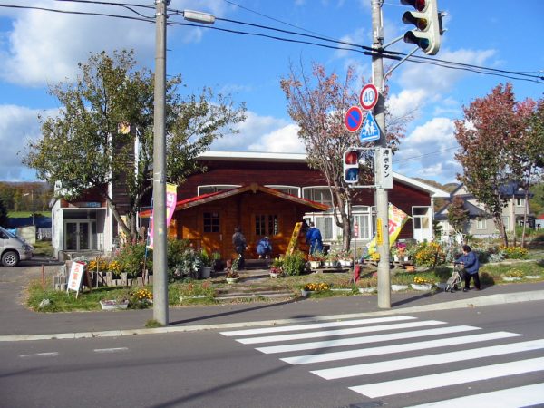 赤茶色の建物外観。玄関前に花壇や掲示板が配置され、入居者が活動している様子が見られます。